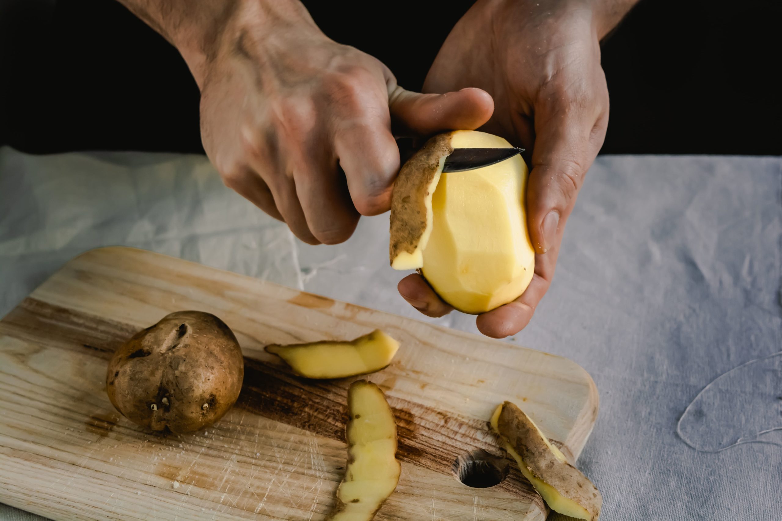 Chef-peeling-potatoes-on-wooden-cutting-board-1-scaled.jpeg